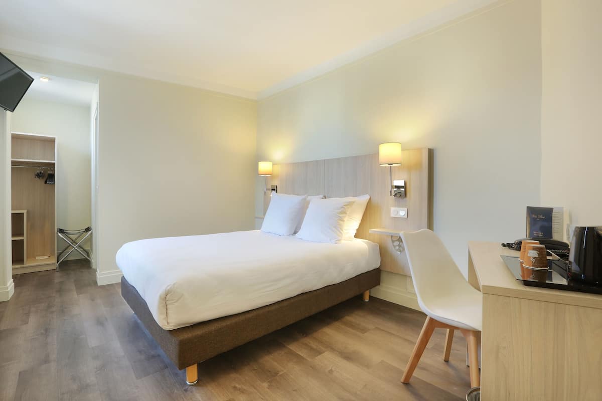 A hotel room with a bed, bedside lamps, a desk with a coffee machine, and a chair.