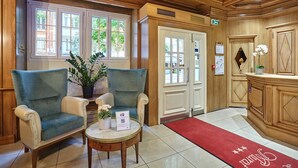 A lobby with two armchairs, a small table with a vase of flowers, and a reception desk.
