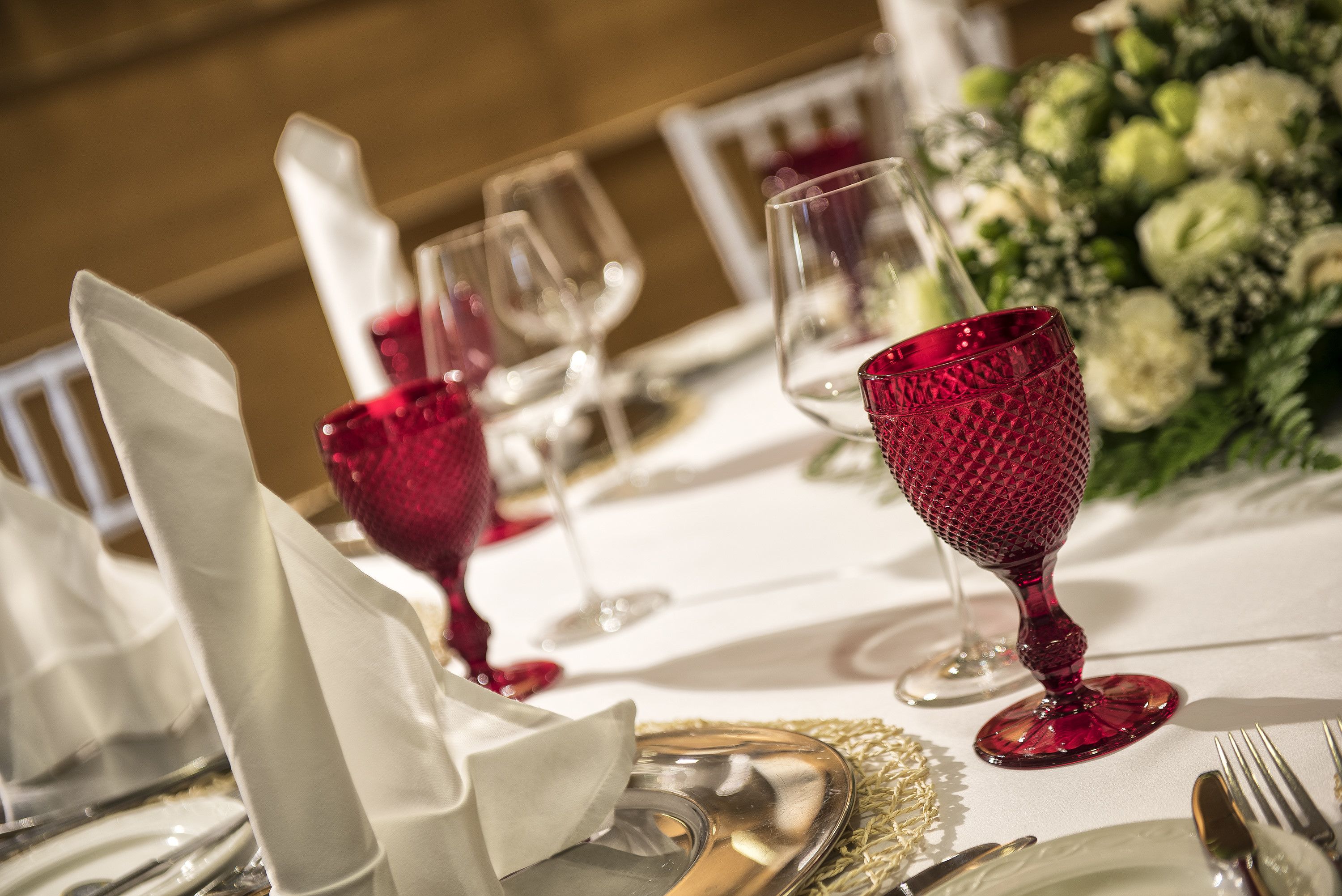 Una mesa dispuesta con servilletas blancas, copas de vino transparentes y un vaso rojo.
