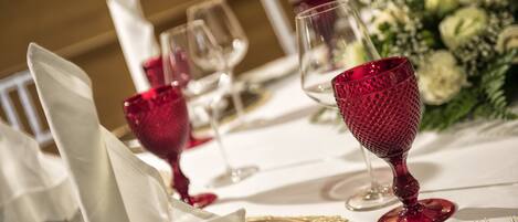 Una mesa dispuesta con servilletas blancas, copas de vino transparentes y un vaso rojo.
