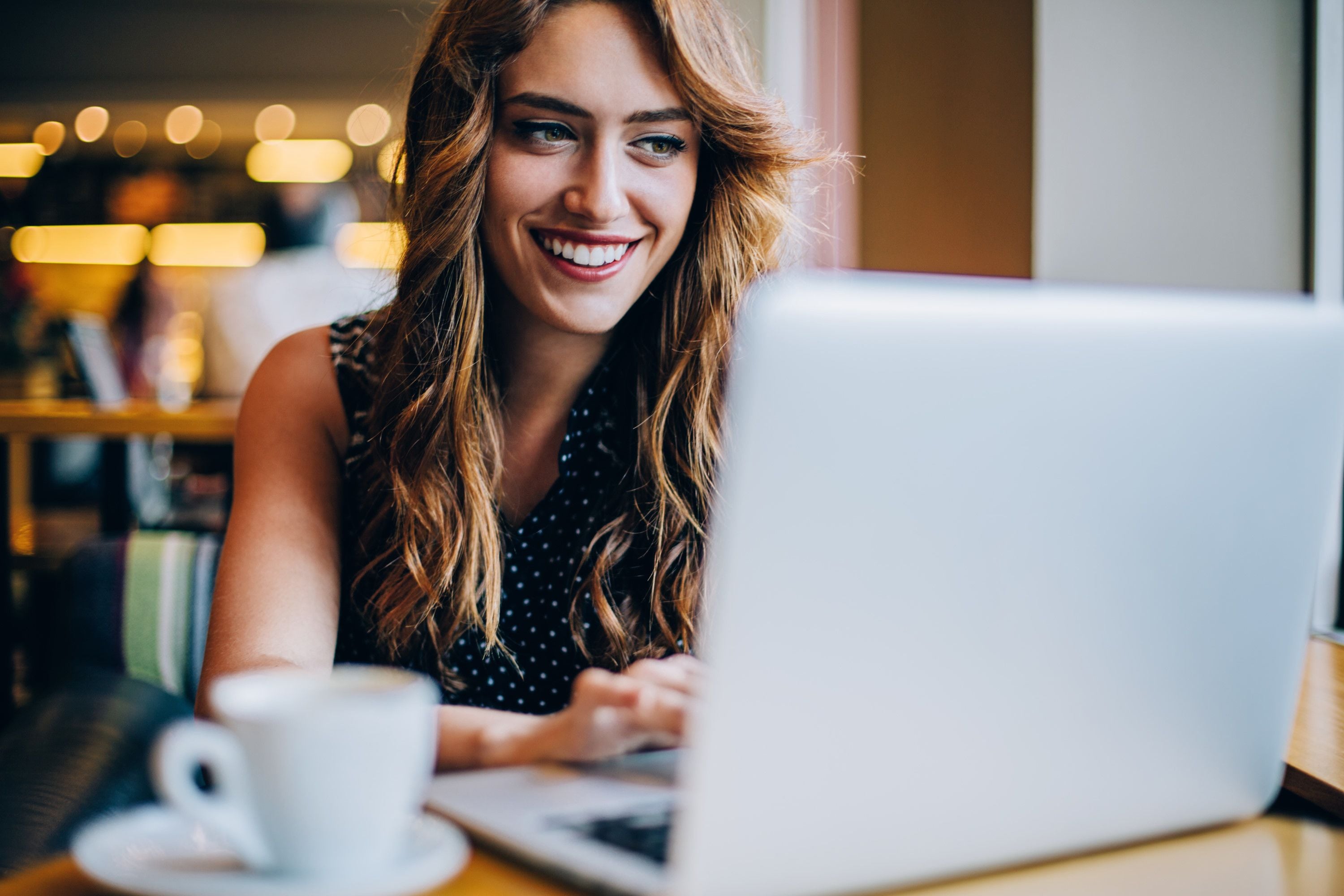 Una persona sentada a una mesa con una computadora portátil y una taza de café.