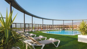 A rooftop pool area with sun loungers and artificial grass, surrounded by a curved glass railing. - Elba Vecindario Aeropuerto Business & Convention Hotel (Santa Lucia)