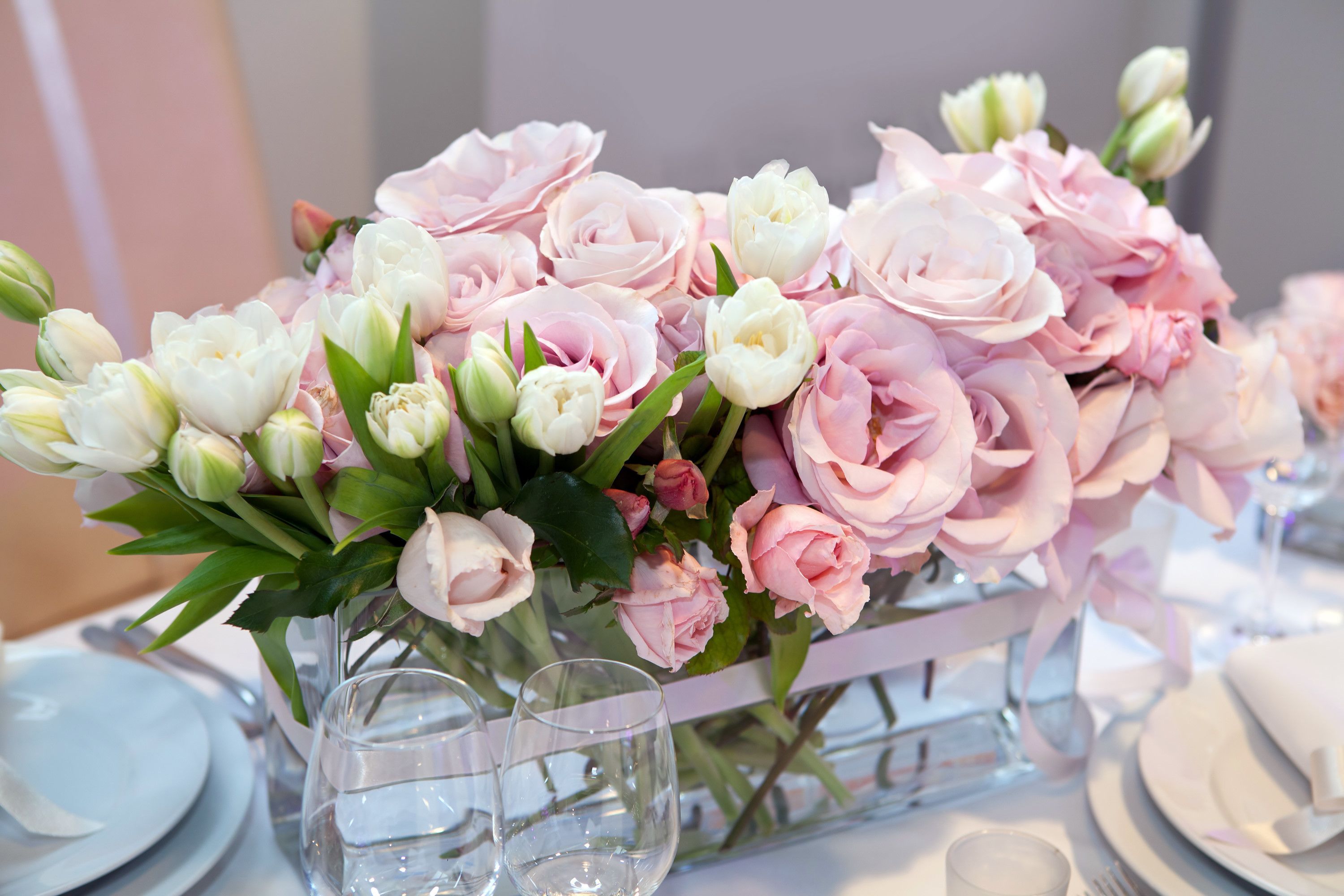 A table set with a vase of pink and white flowers, clear glasses, and plates.