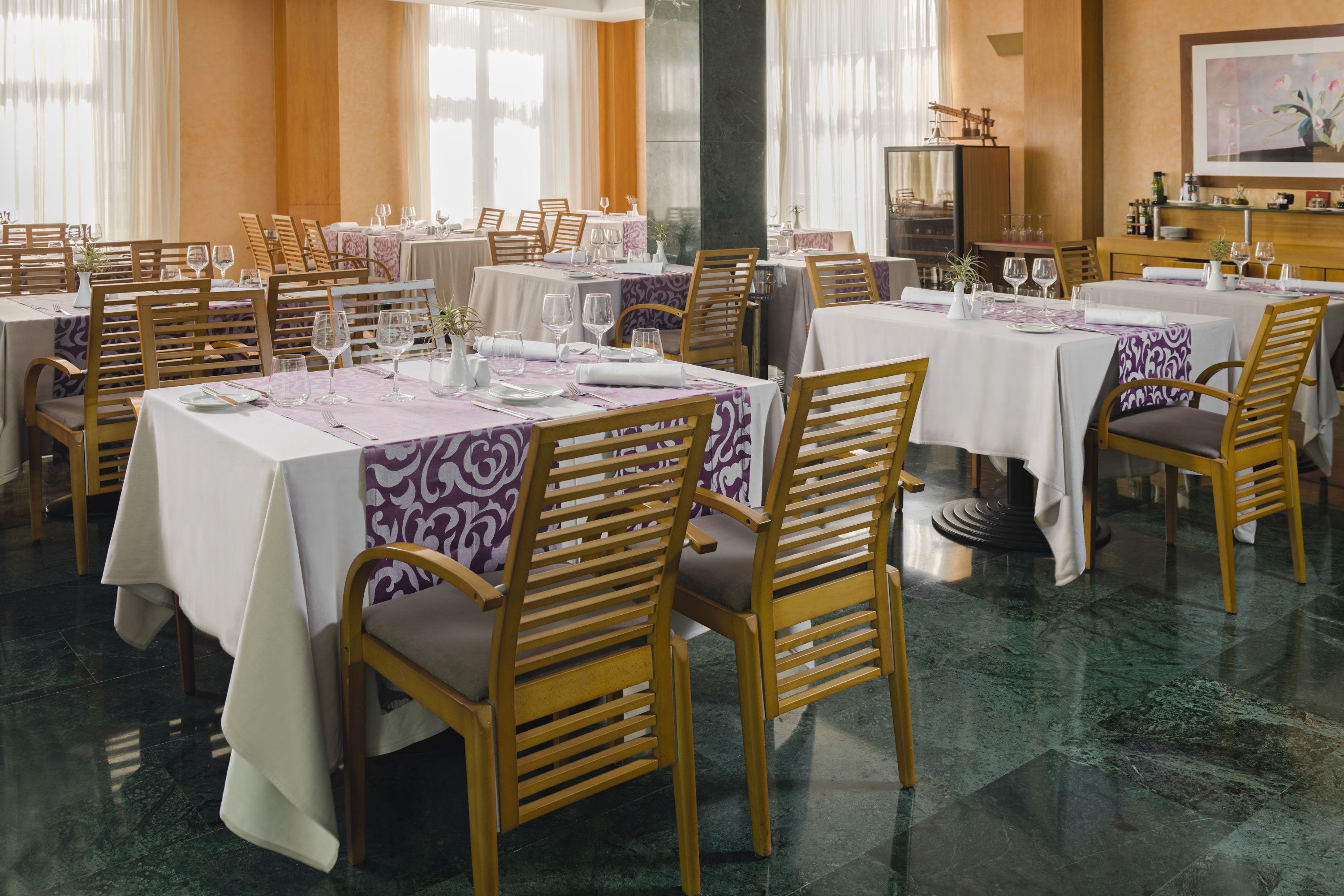 Un restaurant doté de nombreuses tables et chaises, chacune étant recouverte d’une nappe blanche et agrémentée de serviettes violettes.