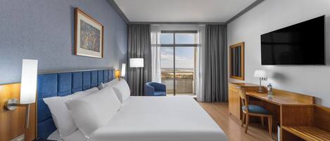 Habitación de hotel con una cama grande, un escritorio, una silla, un televisor y una ventana con cortinas.