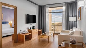 A modern hotel room with a bed, a desk, a TV, a glass table, a sofa, and a balcony with curtains. - Elba Vecindario Aeropuerto Business & Convention Hotel (Santa Lucia)