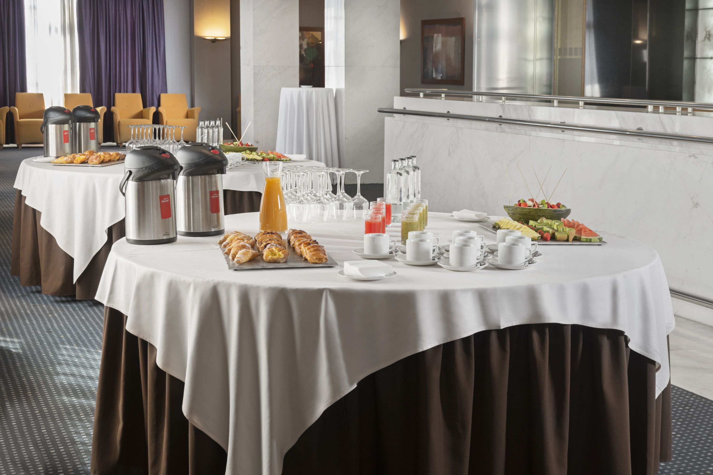 A breakfast buffet with various food items, hot beverages, and glassware on a round table.