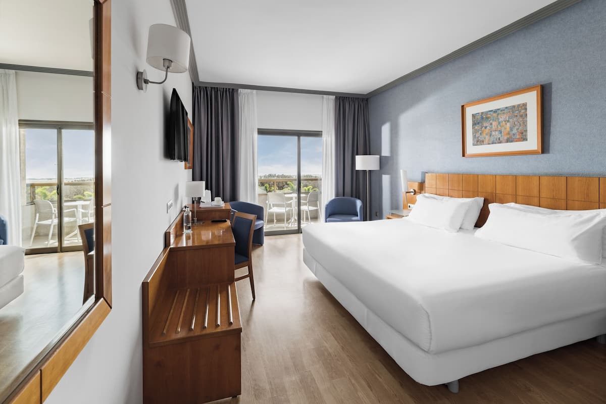 Une chambre d’hôtel avec un grand lit, un bureau, une chaise, une télévision et un balcon avec vue.