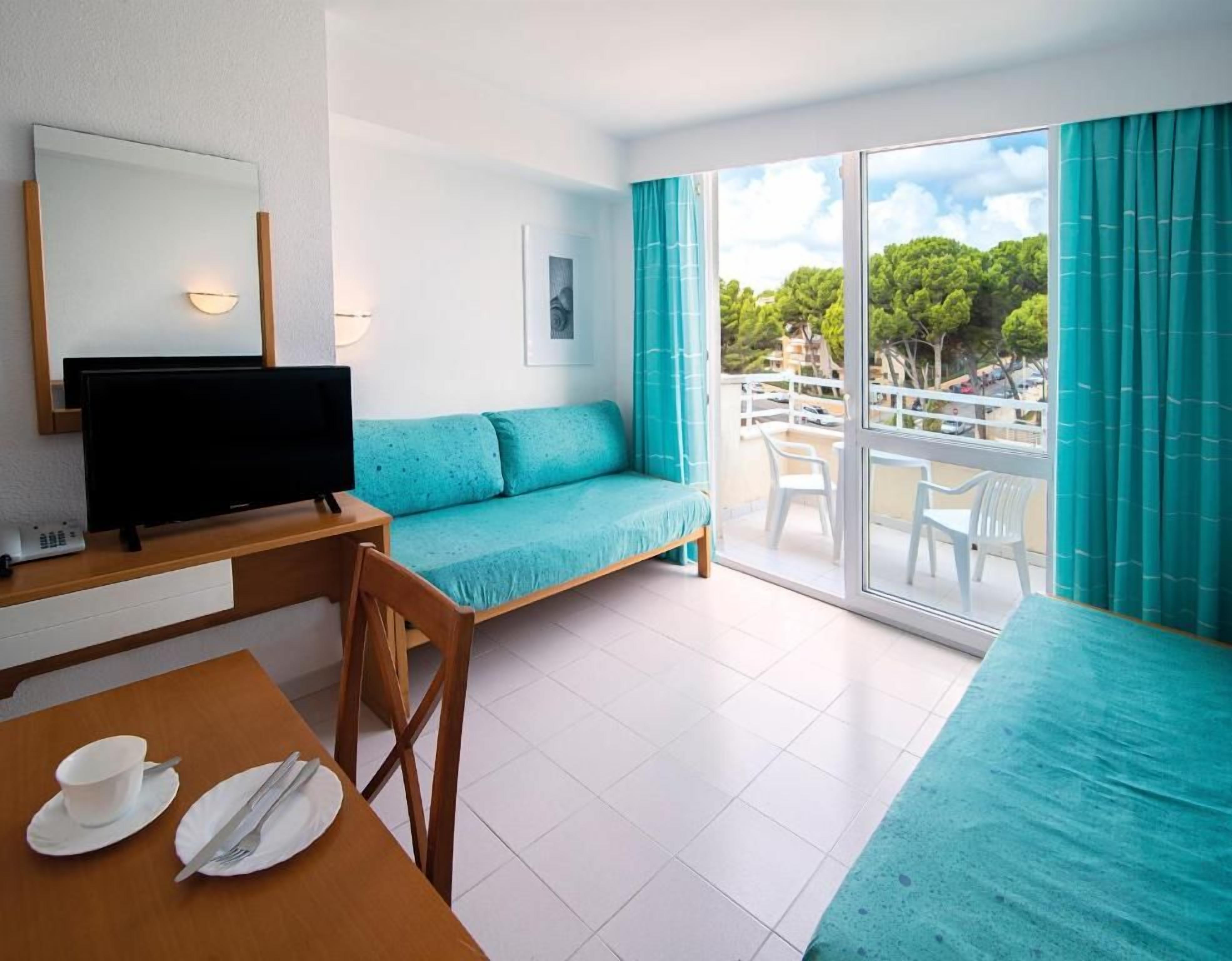 A hotel room with a sofa, a TV, a dining table with cutlery, and a balcony with a view.