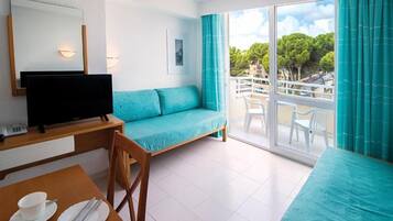 A hotel room with a sofa, a TV, a dining table with cutlery, and a balcony with a view.