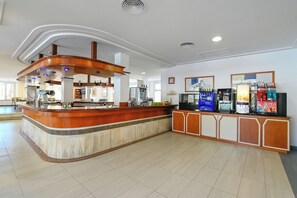 A hotel reception area with a curved wooden counter, a coffee machine, and a water dispenser. - Club Hotel Cala Ratjada (Capdepera)