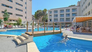 Una piscina con cubierta de madera y sillas de descanso, rodeada de edificios de varios pisos con balcones.