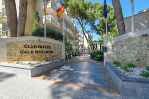 A Club Hotel entrance with a stone wall, a sign, and a pathway leading to the building. - Club Hotel Cala Ratjada (Capdepera)