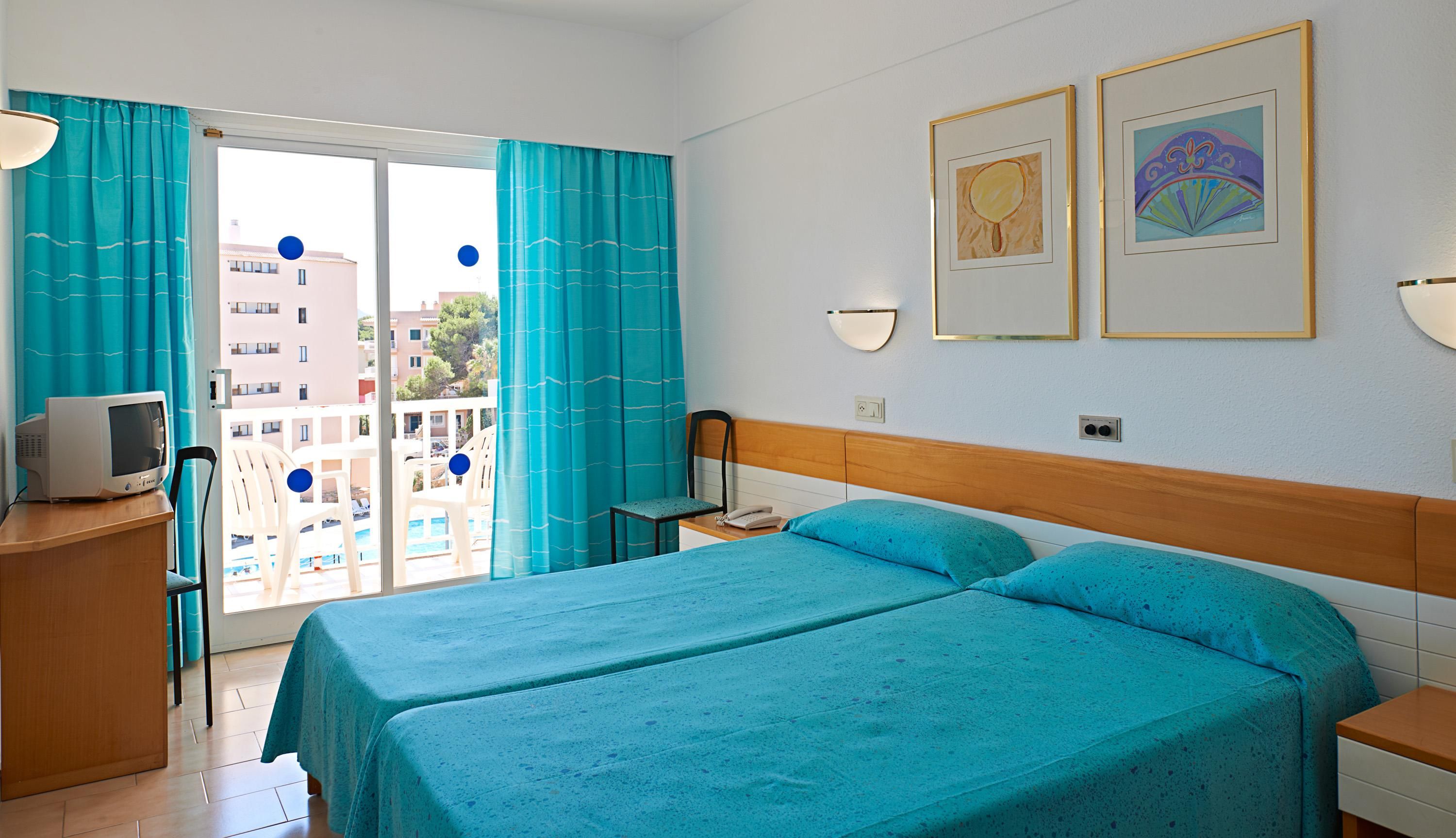 Ein Hotelzimmer mit zwei Betten, einem Schreibtisch mit Computer, einem Stuhl und Blick auf den Balkon.