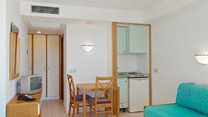Una habitación compacta con una mesa de comedor, sillas, una kitchenette pequeña, un televisor y un sofá.