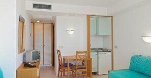 A compact room with a dining table, chairs, a small kitchenette, a television, and a sofa. - Club Hotel Cala Ratjada (Capdepera)