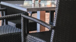 Un área de comedor al aire libre con sillas y mesas de mimbre, algunas con condimentos.