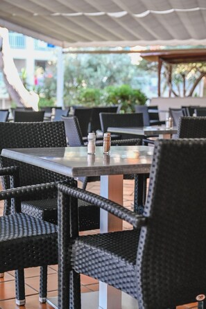 Un área de comedor al aire libre con sillas y mesas de mimbre, algunas con condimentos.