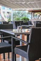 Un área de comedor al aire libre con sillas y mesas de mimbre, algunas con condimentos.