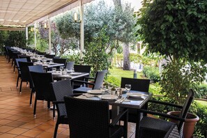 An outdoor dining area with tables and chairs, surrounded by greenery and trees. - Club Hotel Cala Ratjada (Capdepera)