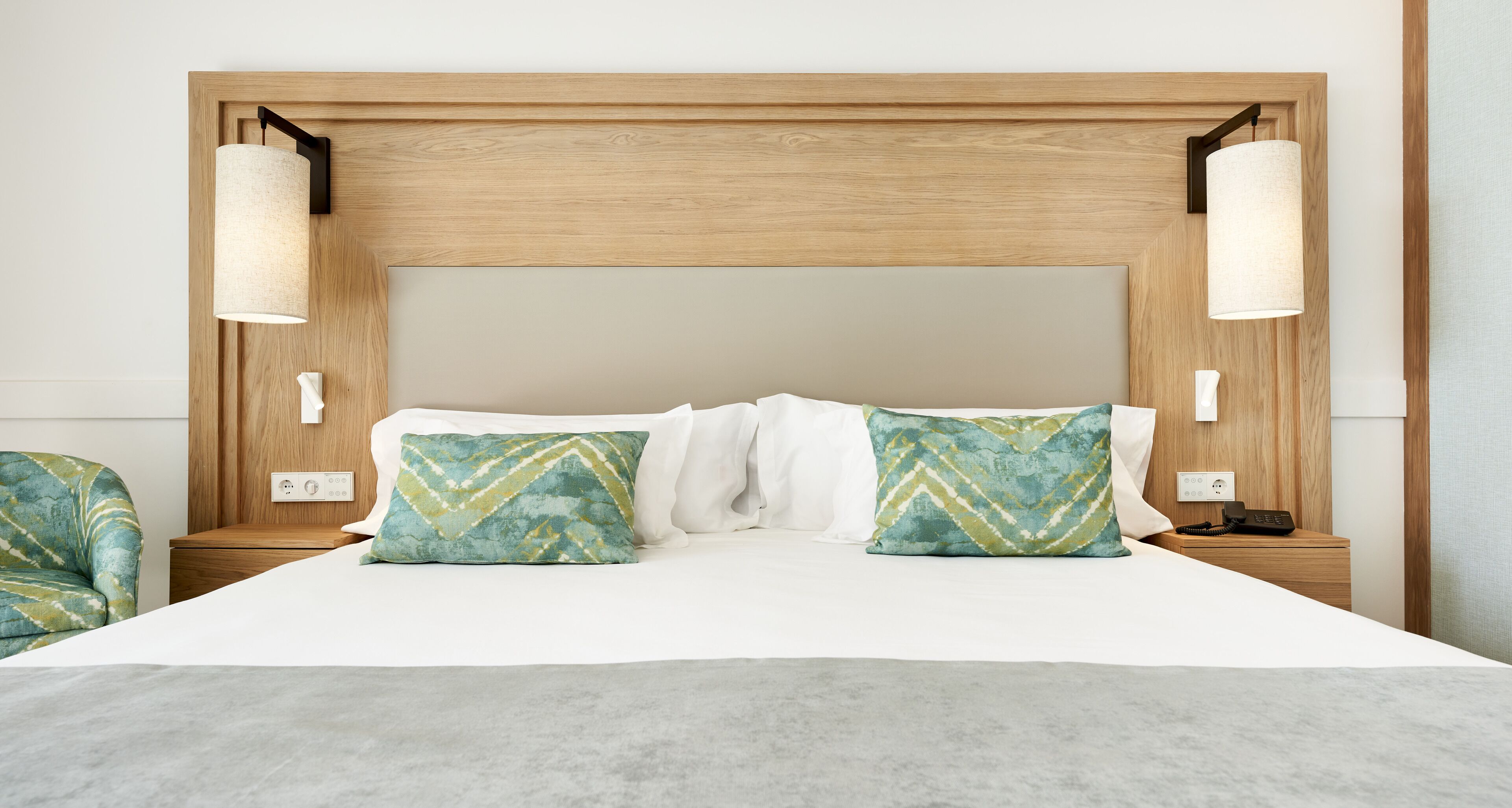 A neatly made bed with a wooden headboard, two bedside lamps, and patterned pillows.