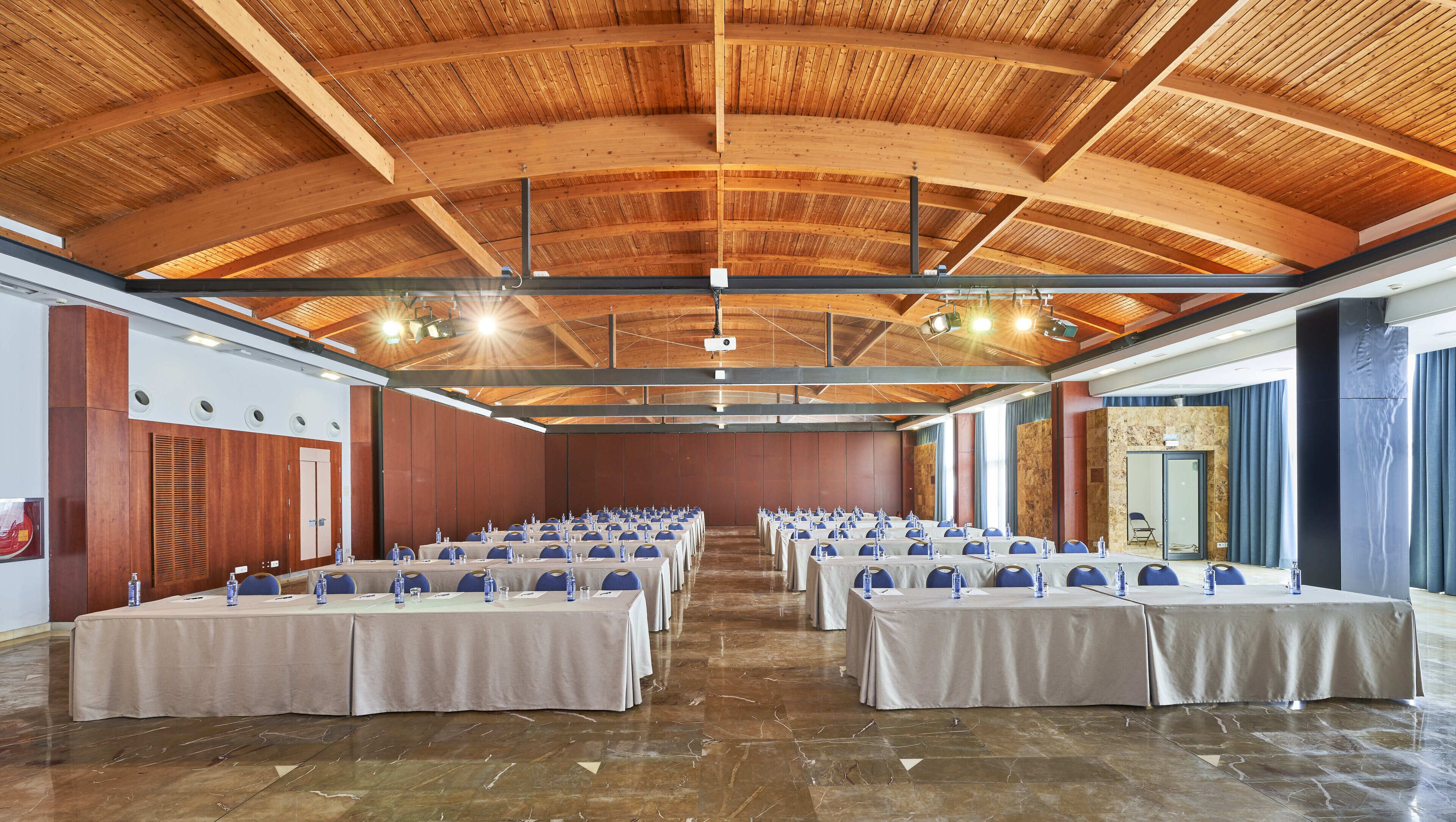 Un amplio salón de conferencias con vigas de madera, suelos de mármol y mesas dispuestas para reuniones.