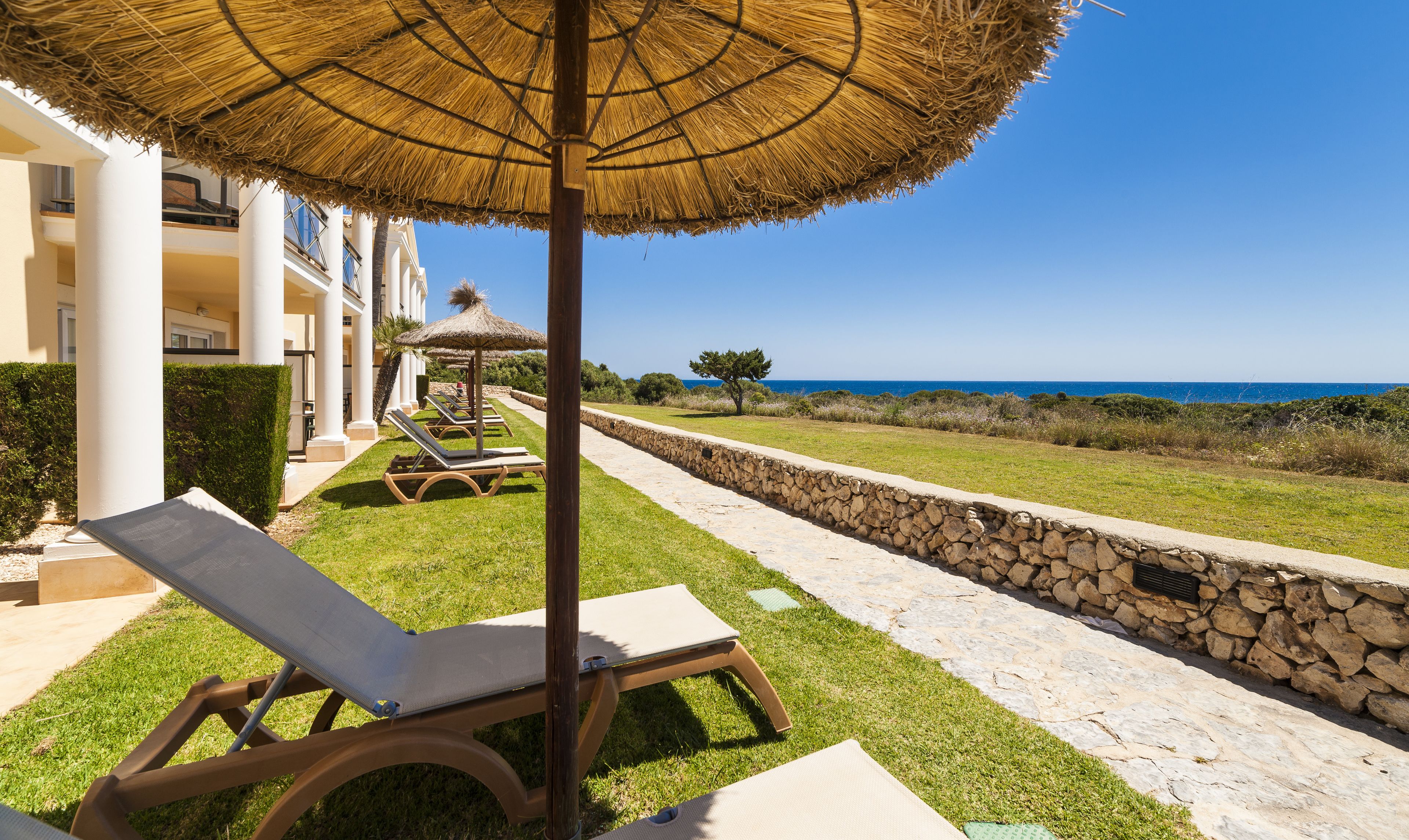 Un resort con un muro de piedra, un espacio con césped y una vista despejada del mar.