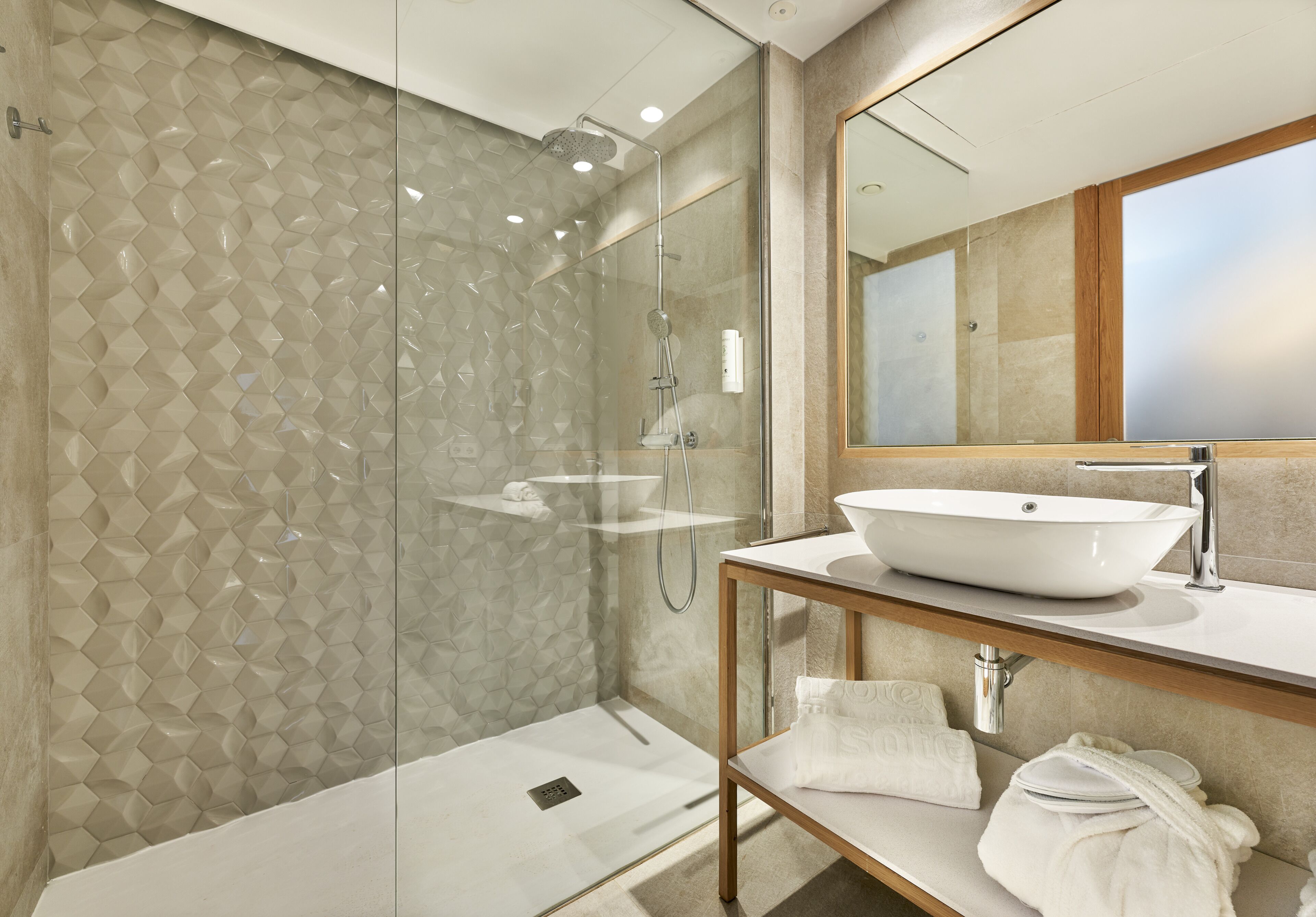 Un baño moderno con ducha de vidrio, un espejo grande y un lavamanos blanco.