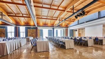 Un salón de conferencias con largas mesas, sillas y un alto techo de madera con vigas a la vista.