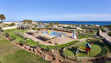 Un resort con zona de piscina, área de juegos para niños y vista al océano.