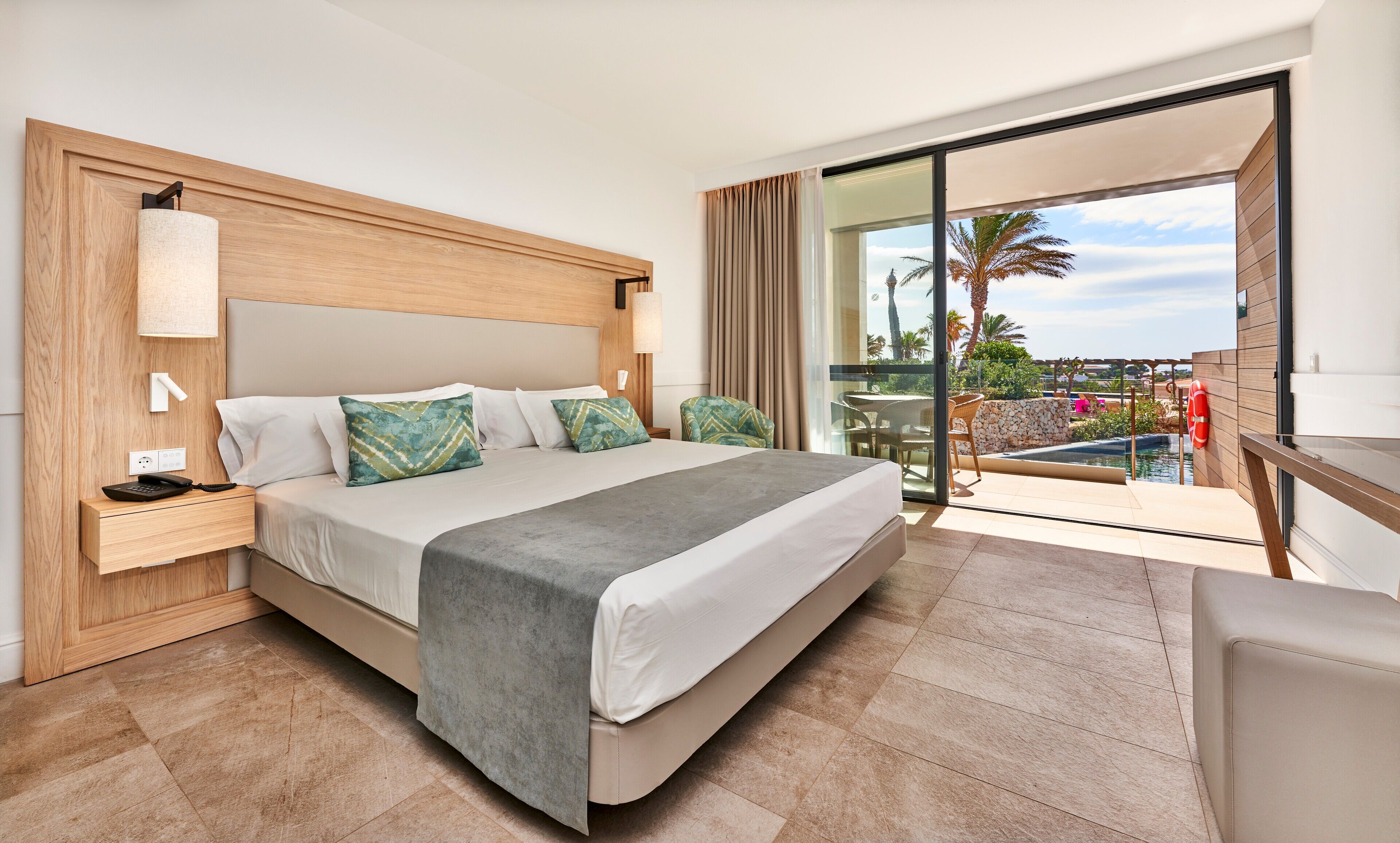 Ein Hotelzimmer mit Bett, Nachttisch und Blick auf einen Pool und Palmen.