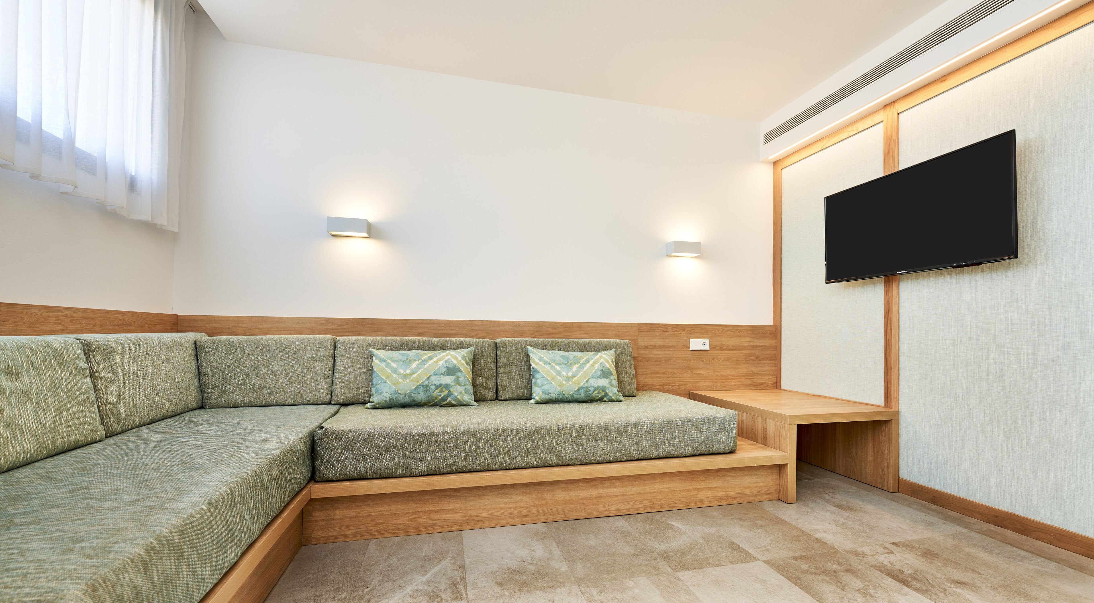 A modern living room with a sectional sofa, wooden bench, and a flat-screen TV mounted on the wall.