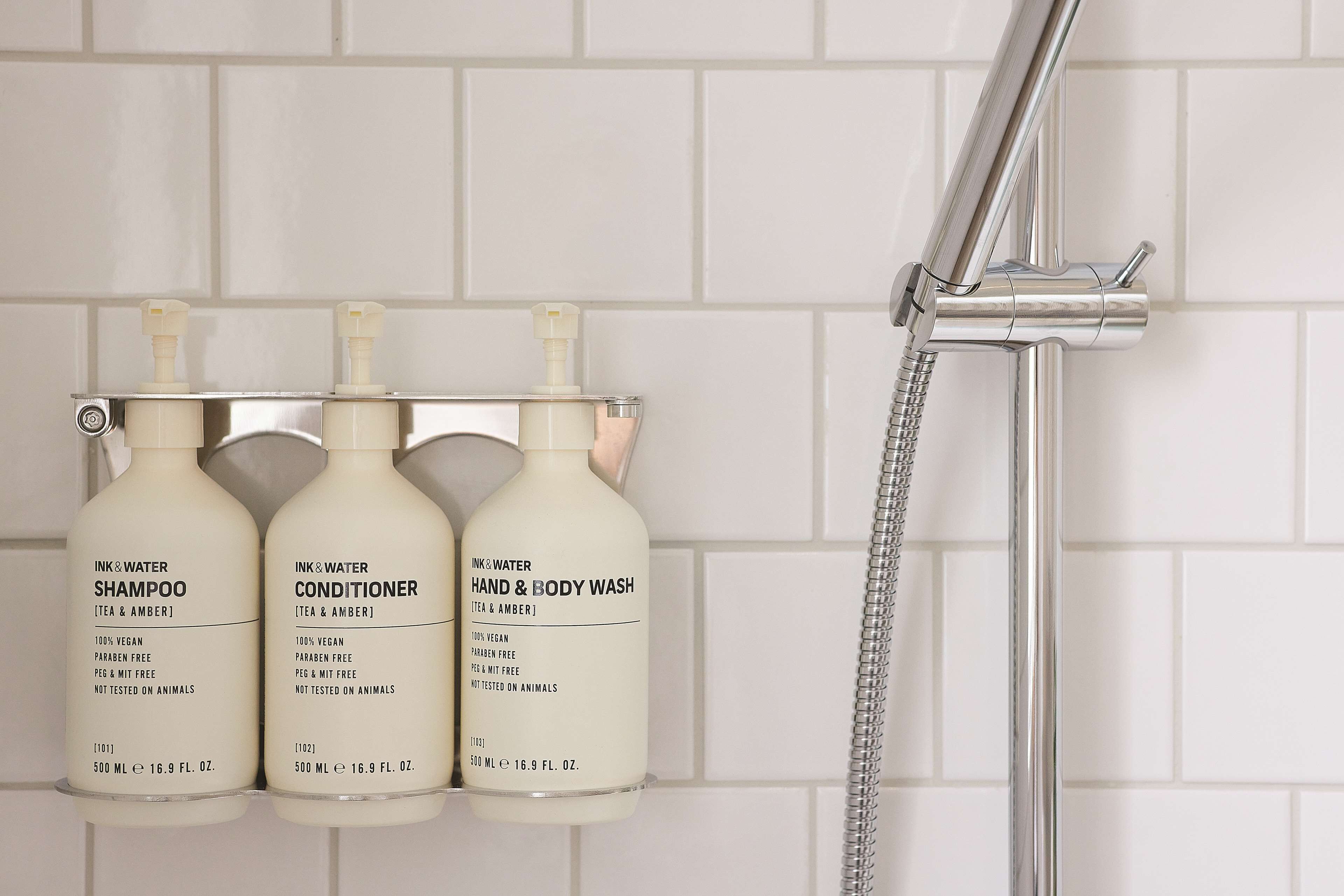 Three bottles of shampoo, conditioner, and body wash on a wall-mounted rack.