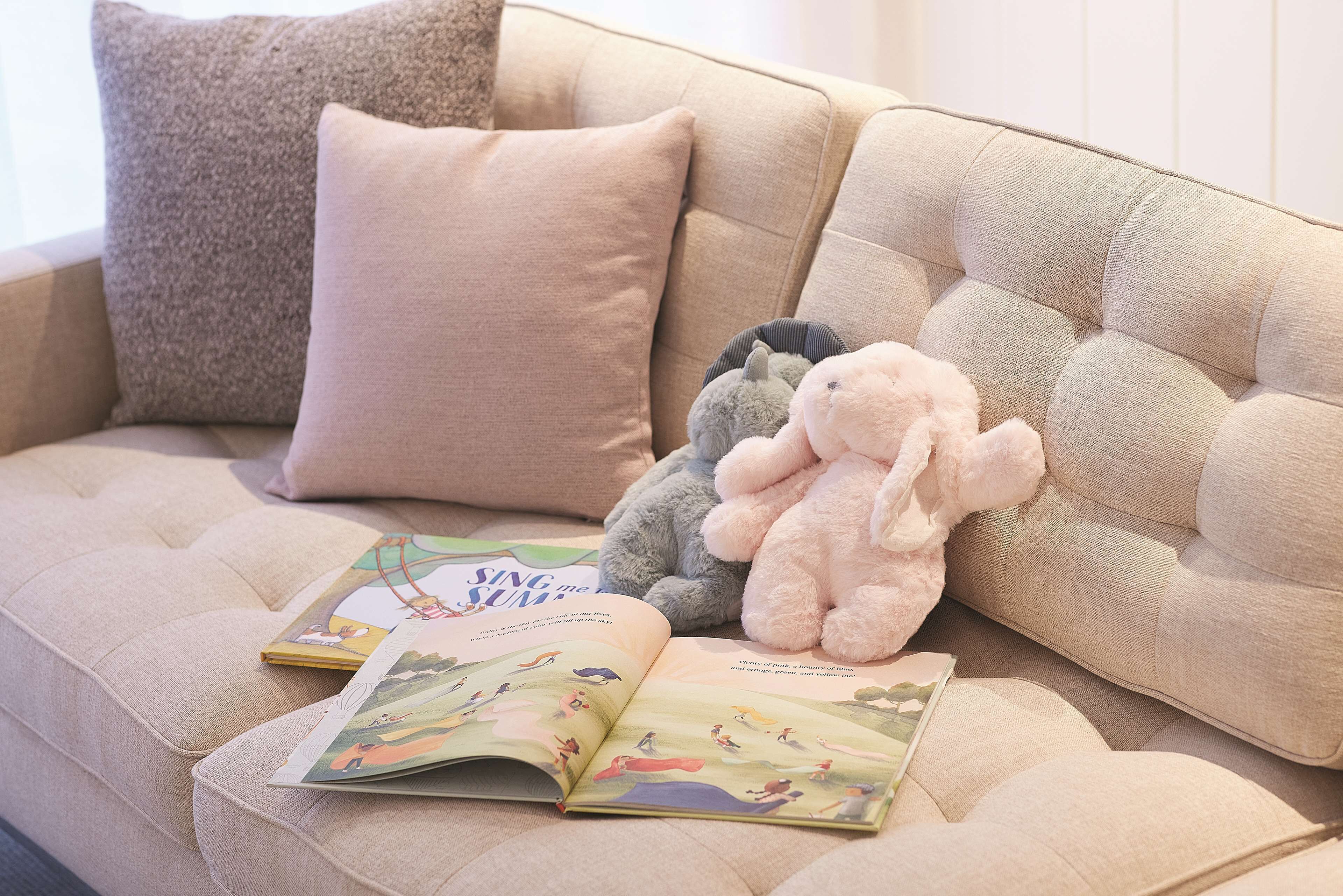 A beige sofa with a book and stuffed animals.