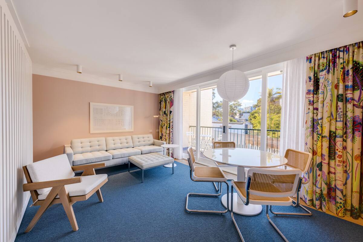 Un salon moderne avec un canapé, des fauteuils, une table à manger et de grandes fenêtres.