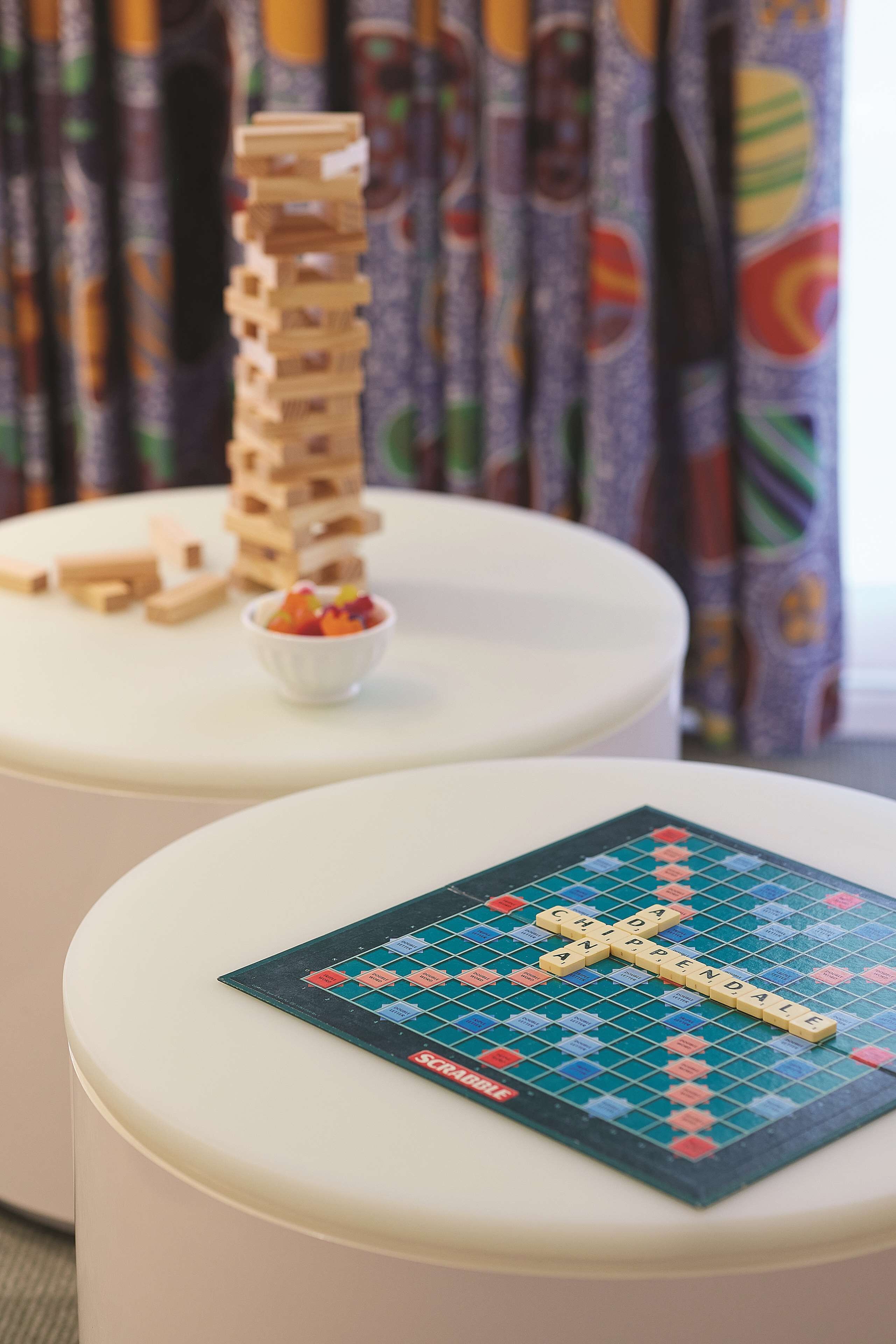 Un jeu de société Scrabble sur une table blanche, avec un présentoir à lettres de Scrabble à côté.