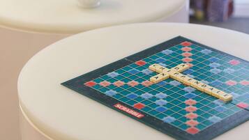 Un jeu de société Scrabble sur une table blanche, avec un présentoir à lettres de Scrabble à côté.