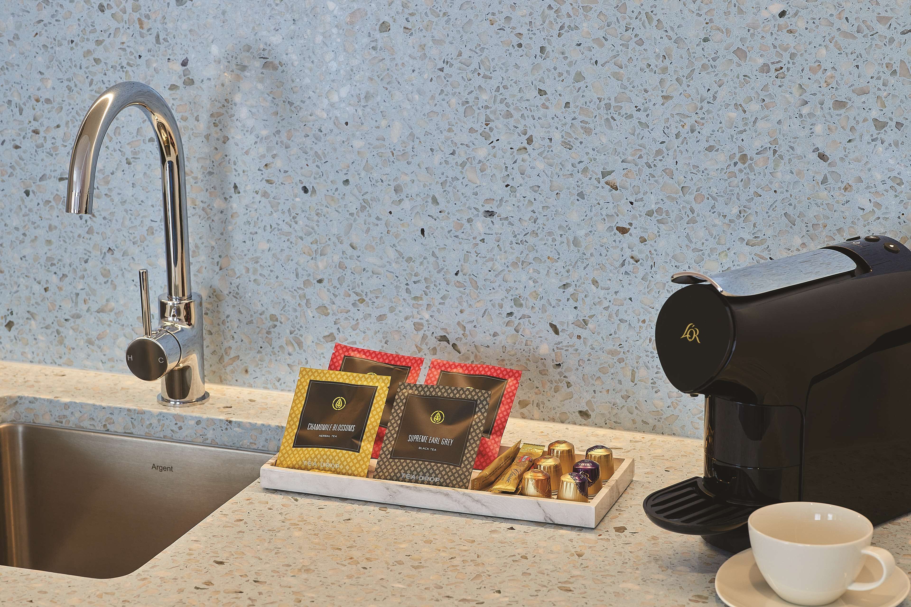 A kitchen counter with a coffee maker, a cup, and a tray of coffee pods.