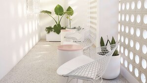 A modern interior with a white color scheme, featuring a seating area with a metal-framed chair and a white sofa, surrounded by potted plants and a white partition with circular cutouts.
