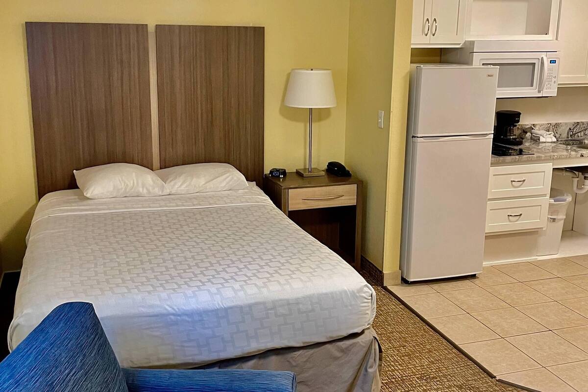 Ein Hotelzimmer mit Bett, Nachttisch mit Lampe, Kühlschrank und einer kleinen Küchenzeile mit Mikrowelle.