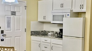 Eine kleine Küche mit weißen Schränken, einer Mikrowelle, einem Kühlschrank und einem Spülbecken.