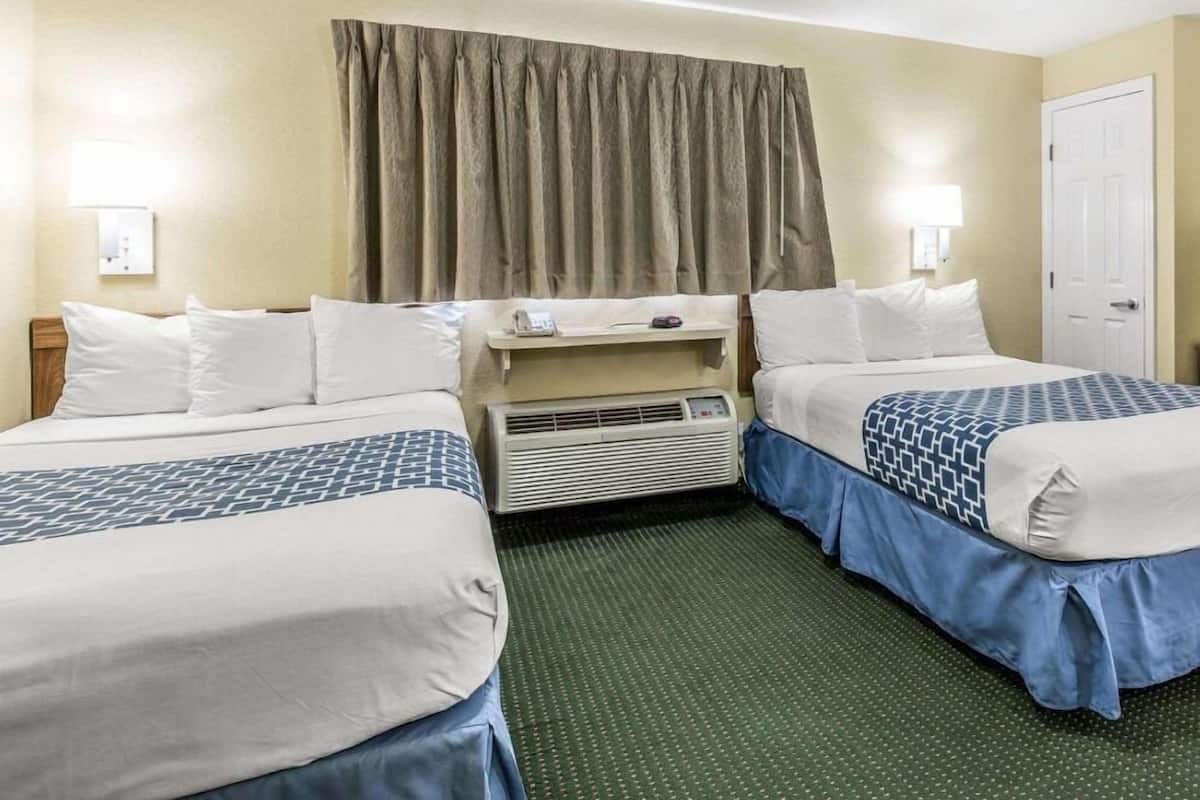 Ein Hotelzimmer mit zwei Betten, einem Schreibtisch, einem Telefon und einer Tür.