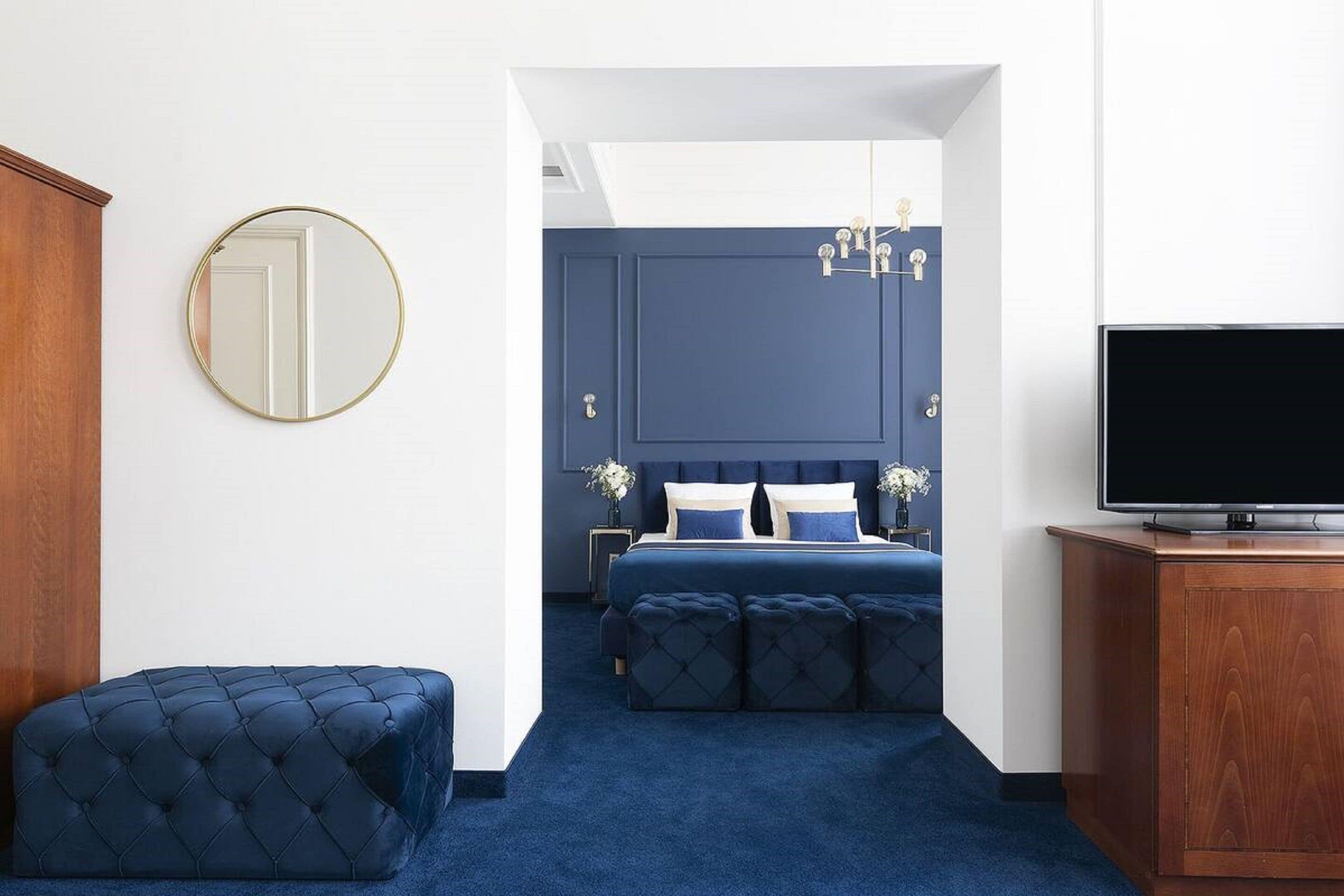 Un dormitorio con una cama grande, un aparador, un televisor y un espejo redondo.