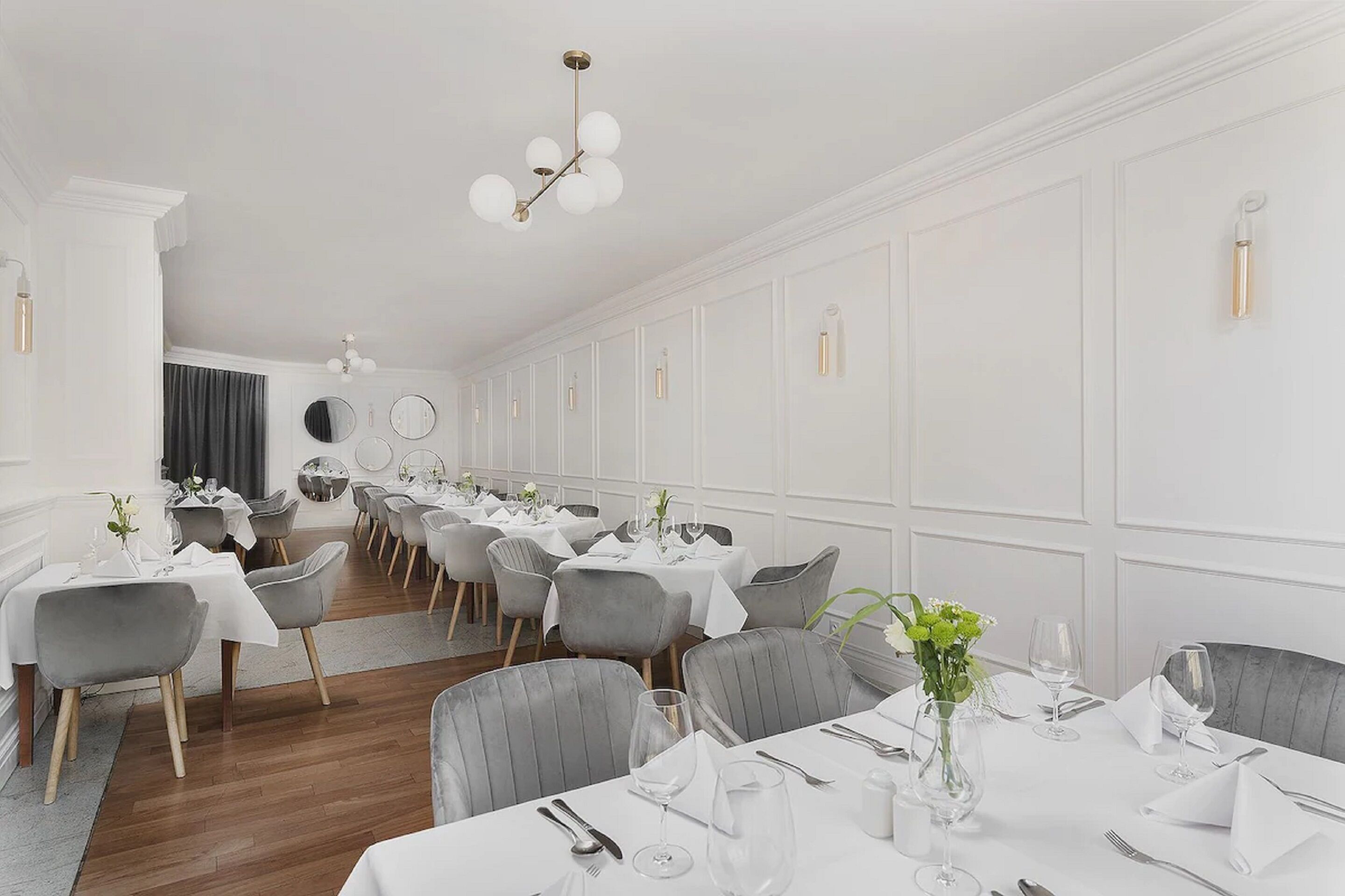 A formal dining room with white walls, grey upholstered chairs, and round tables set for dining.