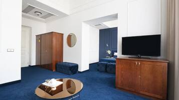 Una sala moderna con alfombra azul, una mesa redonda de centro, un televisor sobre un mueble de madera y un espejo grande en la pared.