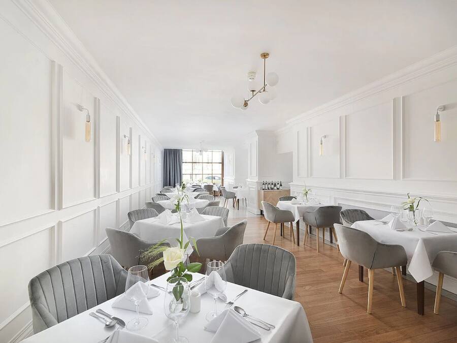A dining area with multiple tables set for service, featuring white tablecloths and grey chairs.