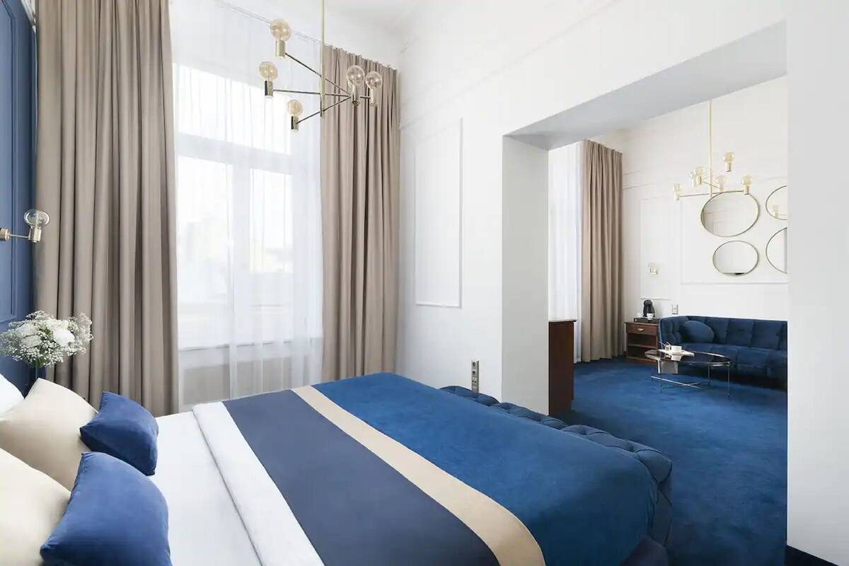A modern hotel room with a large bed, a smaller bed, a desk, and a sofa.
