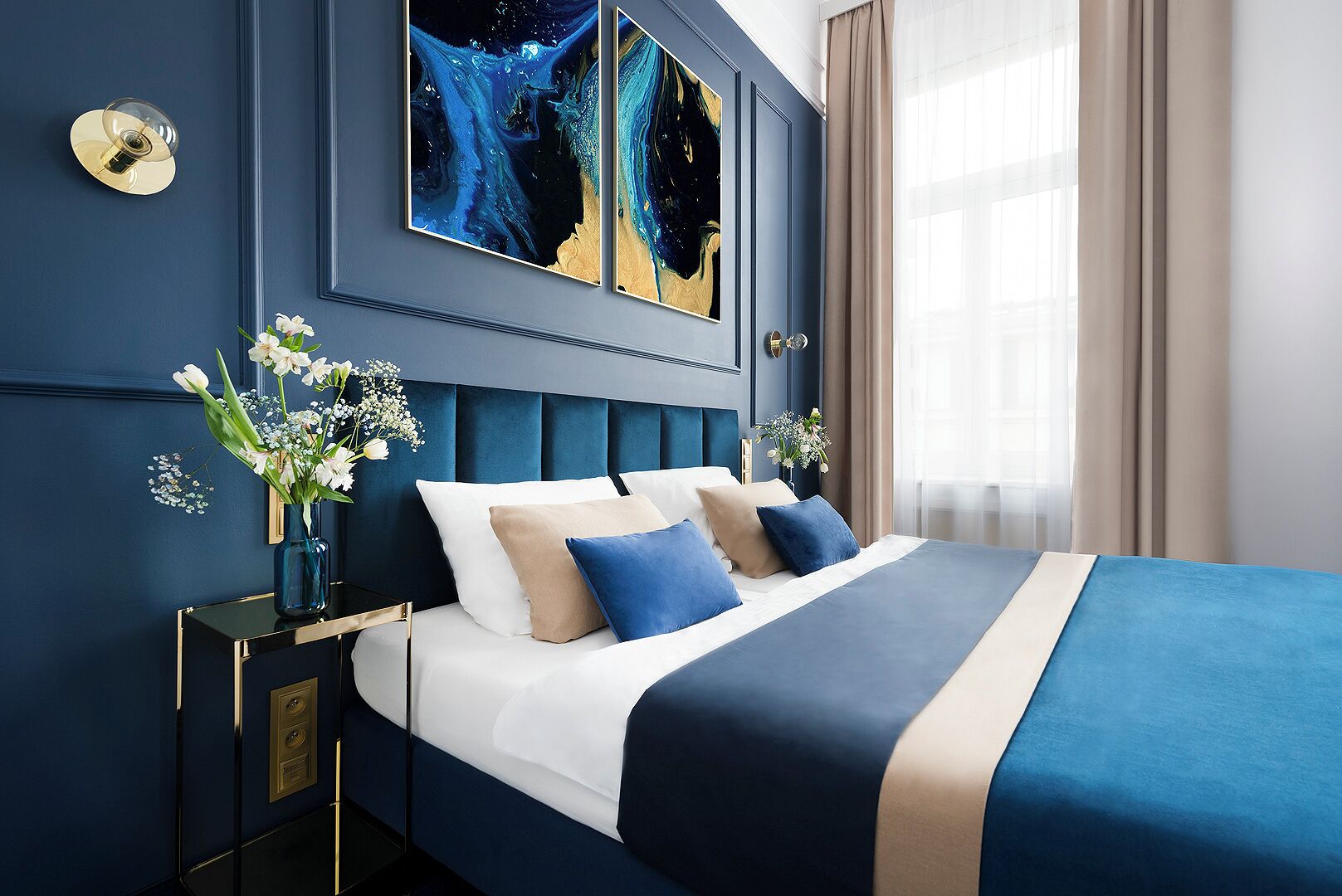 A bedroom with a bed, a nightstand, a vase with flowers, and a painting on the wall.