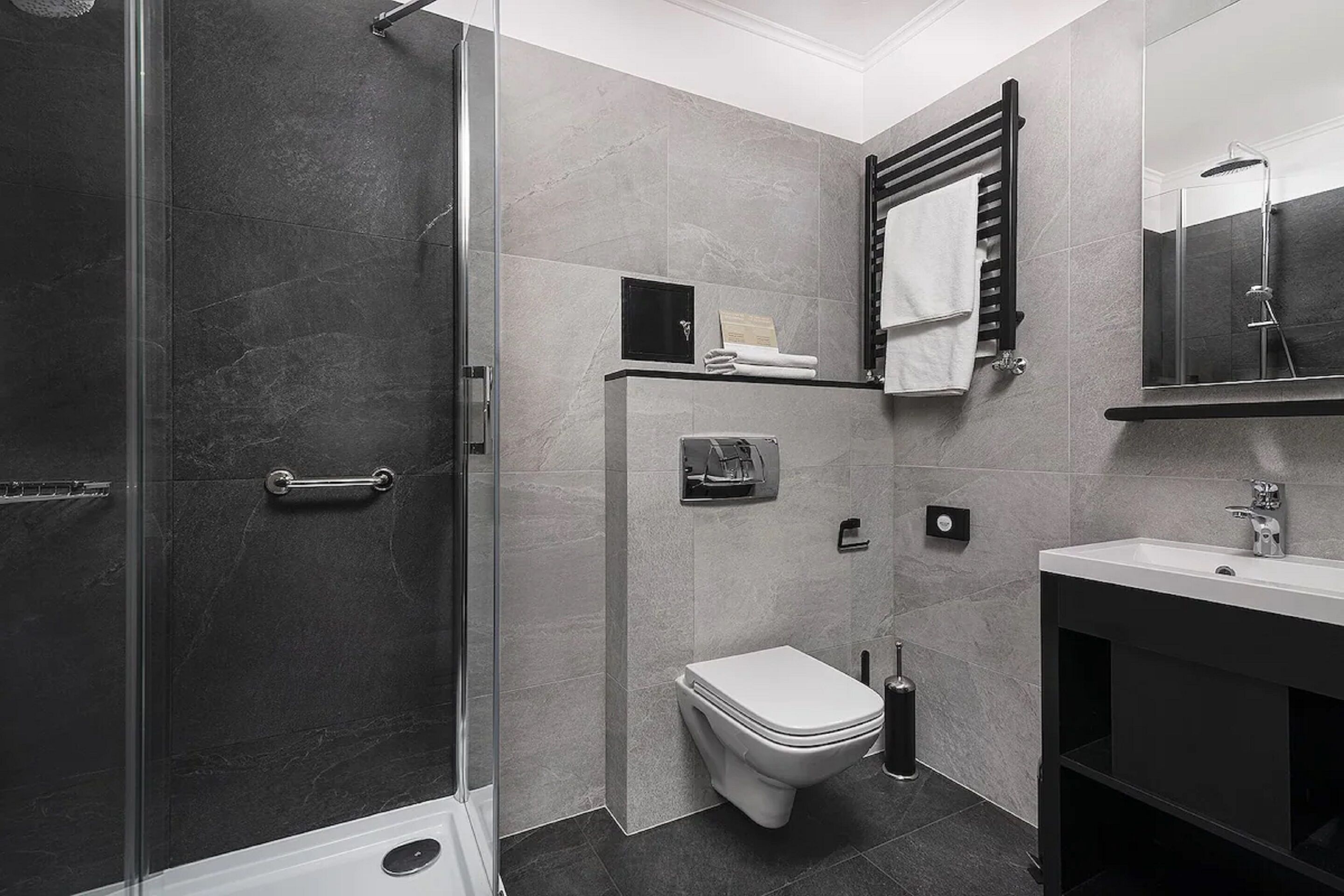 A modern bathroom with a glass shower enclosure, a toilet, a sink, and a towel rack.
