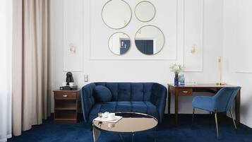 A hotel room with a blue sofa, a round coffee table, a desk with a chair, and three wall-mounted mirrors.